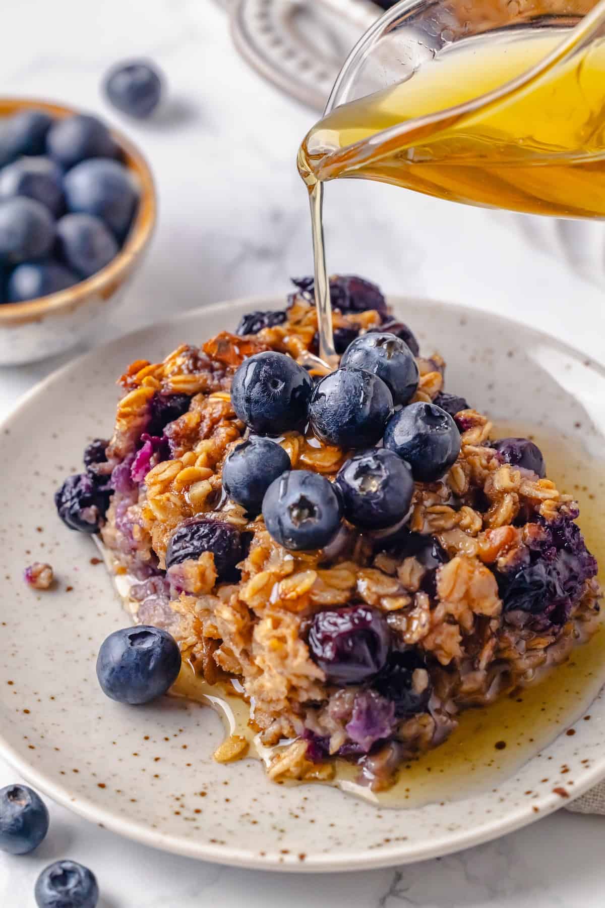 Pouring maple syrup onto portion of blueberry baked oatmeal on plate