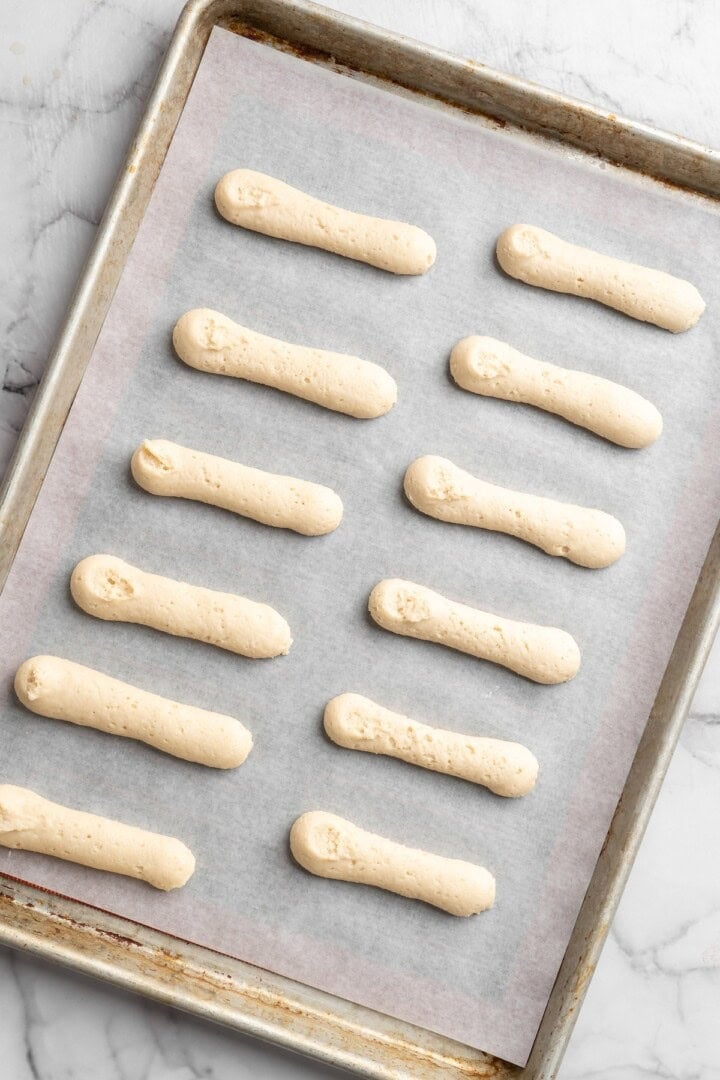 Overhead view of unbaked vegan ladyfingers on parchment-lined sheet pan