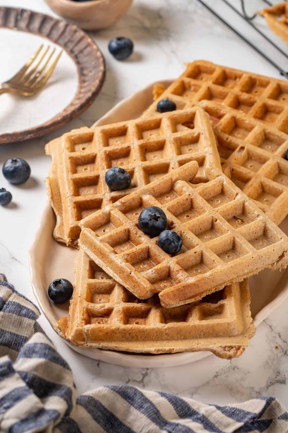 Protein waffles help you power through your morning with 10 grams of protein! They’re fluffy and delicious, with some extra satisfaction. Platter of protein waffles topped with blueberries
