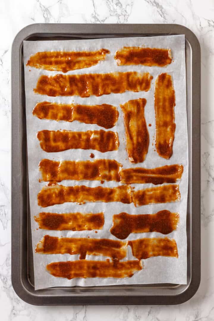 Rice paper is the secret for ultra crispy vegan bacon! This recipe is smoky, sweet, and savoury, and it's incredibly easy to make too. Overhead view of vegan rice paper bacon on parchment-lined baking sheet before baking