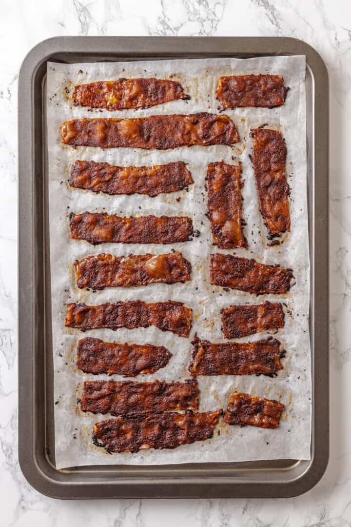 Rice paper is the secret for ultra crispy vegan bacon! This recipe is smoky, sweet, and savoury, and it's incredibly easy to make too. Overhead view of rice paper bacon on parchment-lined baking sheet
