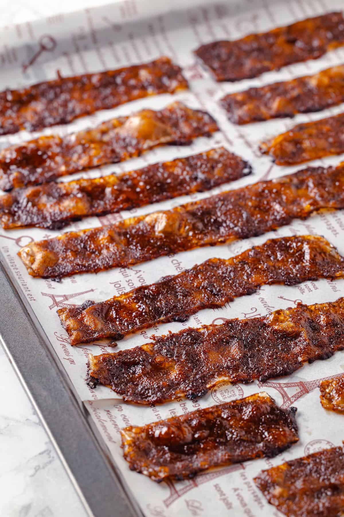 Rice paper is the secret for ultra crispy vegan bacon! This recipe is smoky, sweet, and savoury, and it's incredibly easy to make too. Crispy vegan bacon on parchment-lined baking sheet