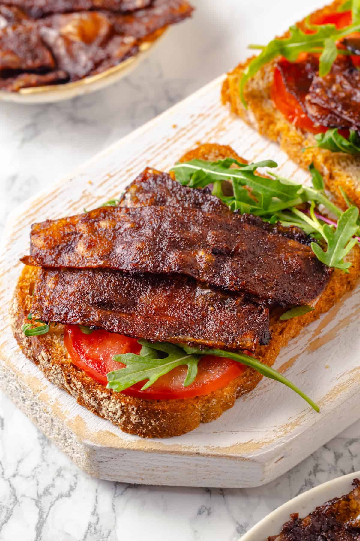 Rice paper is the secret for ultra crispy vegan bacon! This recipe is smoky, sweet, and savoury, and it's incredibly easy to make too. Crispy vegan bacon on bread with tomato and arugula