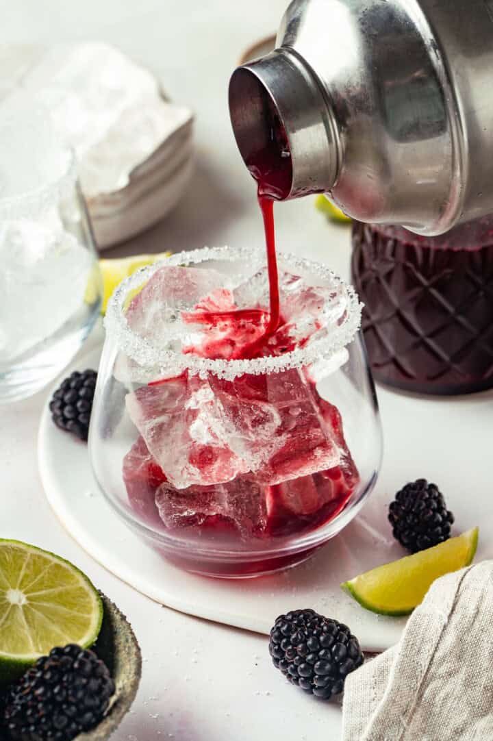 Pouring blackberry margarita into glass with salted rim