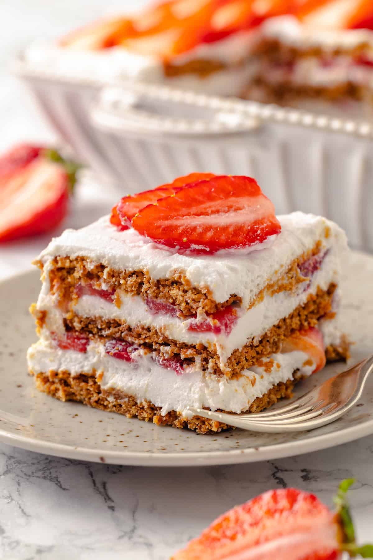 This strawberry icebox cake is cool, creamy, and super easy to make, with vegan whipped cream, fresh strawberries, and graham crackers. Yum! Slice of strawberry icebox cake on plate with fork