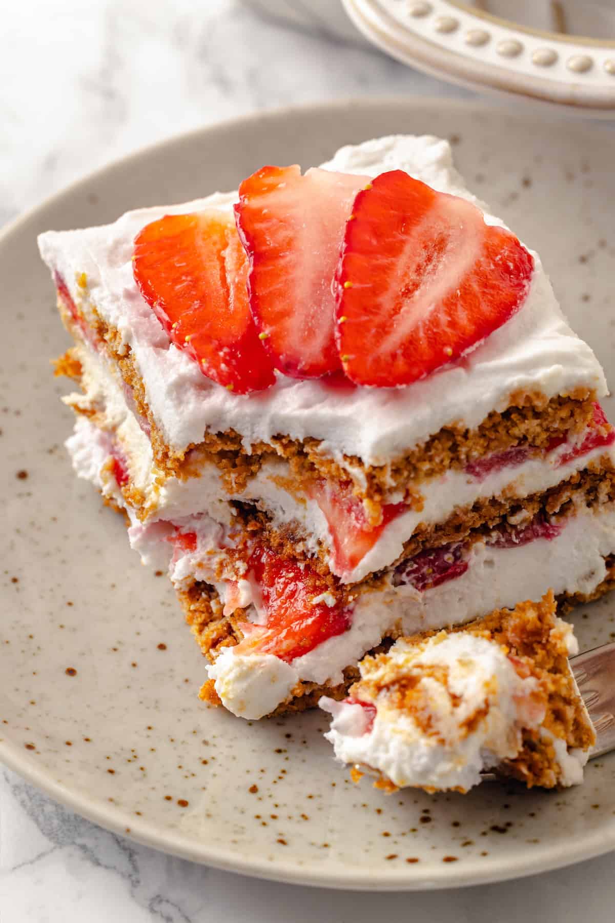 Slice of strawberry icebox cake on plate with corner on fork