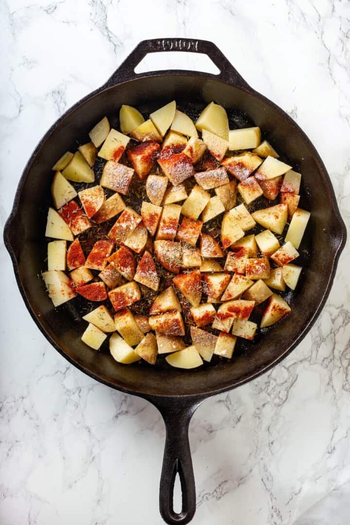 Overhead view of potatoes in skillet with seasonings added