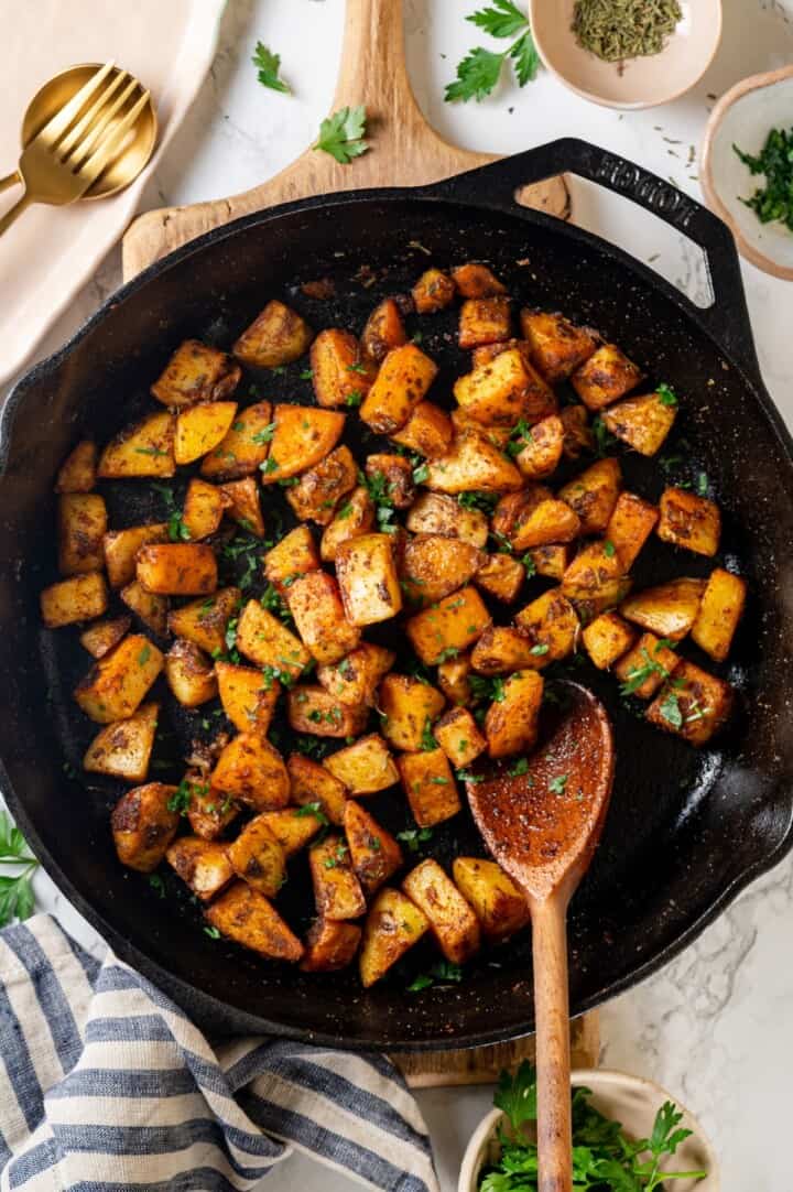 Overhead view of breakfast potatoes in cast iron skillet with wooden spoon