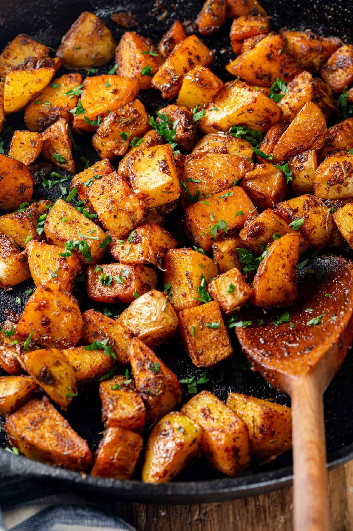 Breakfast potatoes in cast iron skillet with wooden spoon