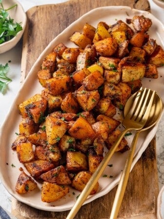 Crispy breakfast potatoes on platter with serving spoon and fork