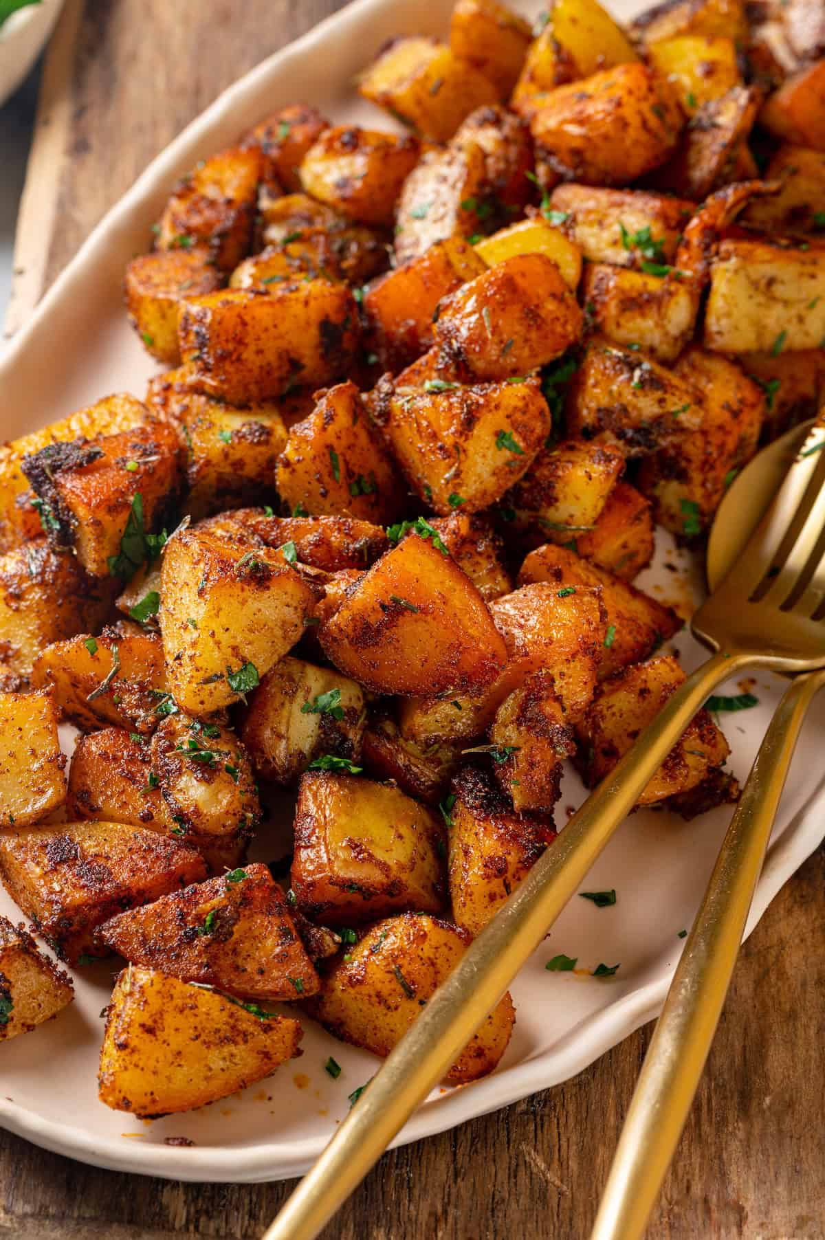 Crispy breakfast potatoes on platter with fork and serving spoon