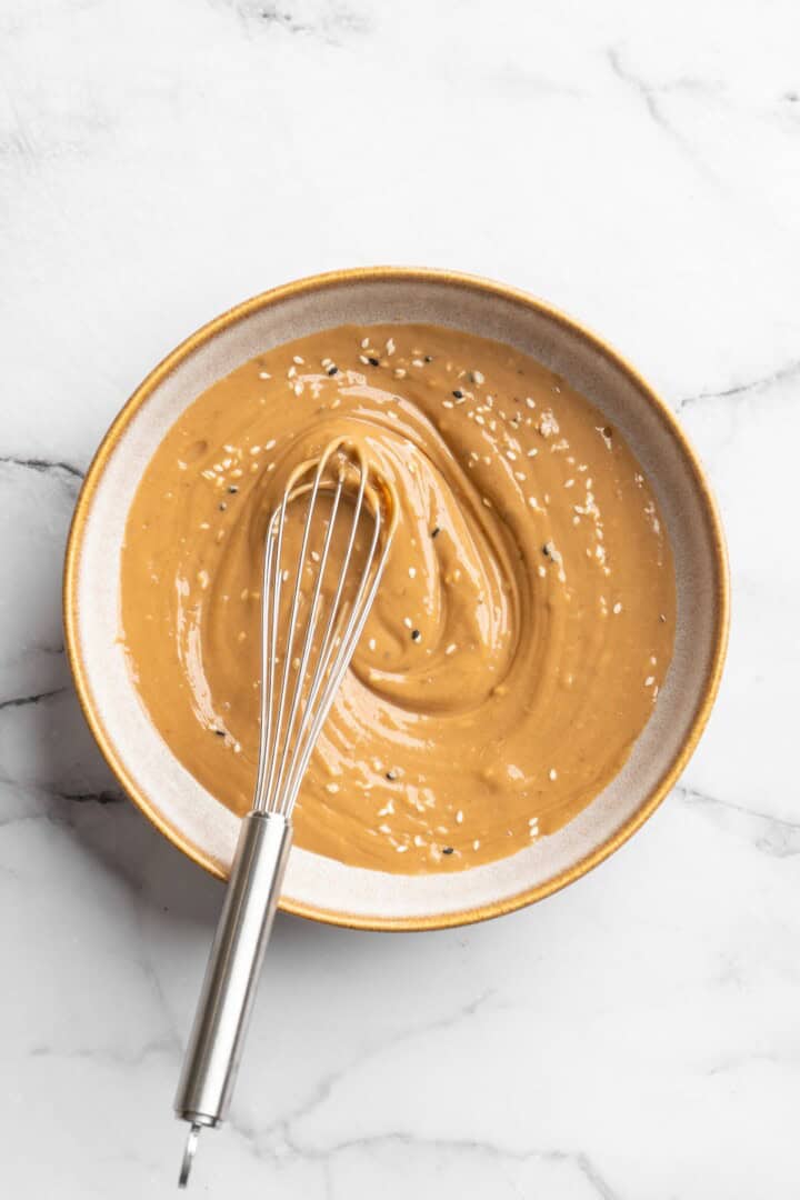 Overhead view of peanut sauce in bowl with whisk