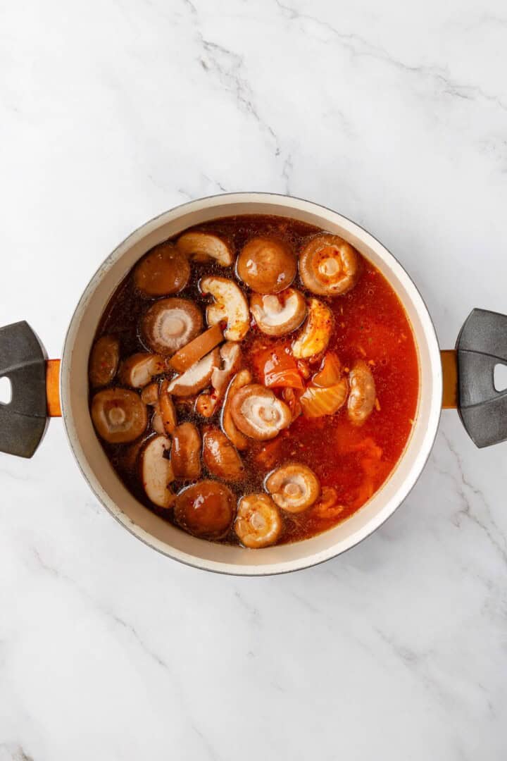Overhead view of mushrooms added to pot for kimchi ramen