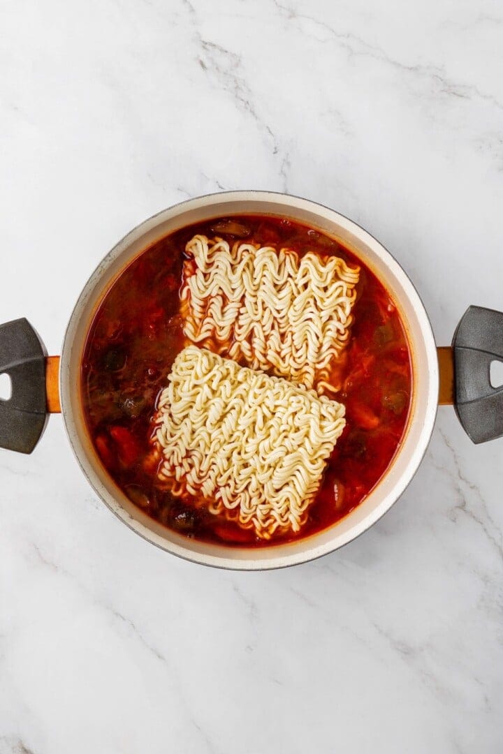 Overhead view of ramen noodles added to pot of kimchi broth