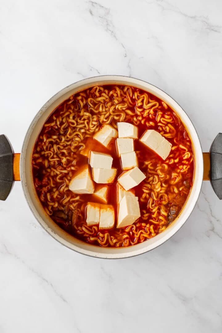 Overhead view of tofu added to pot of kimchi ramen
