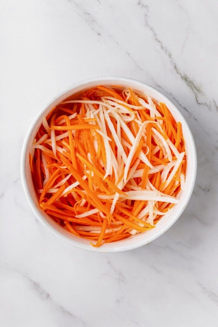 Overhead view of julienned radish and carrot in bowl