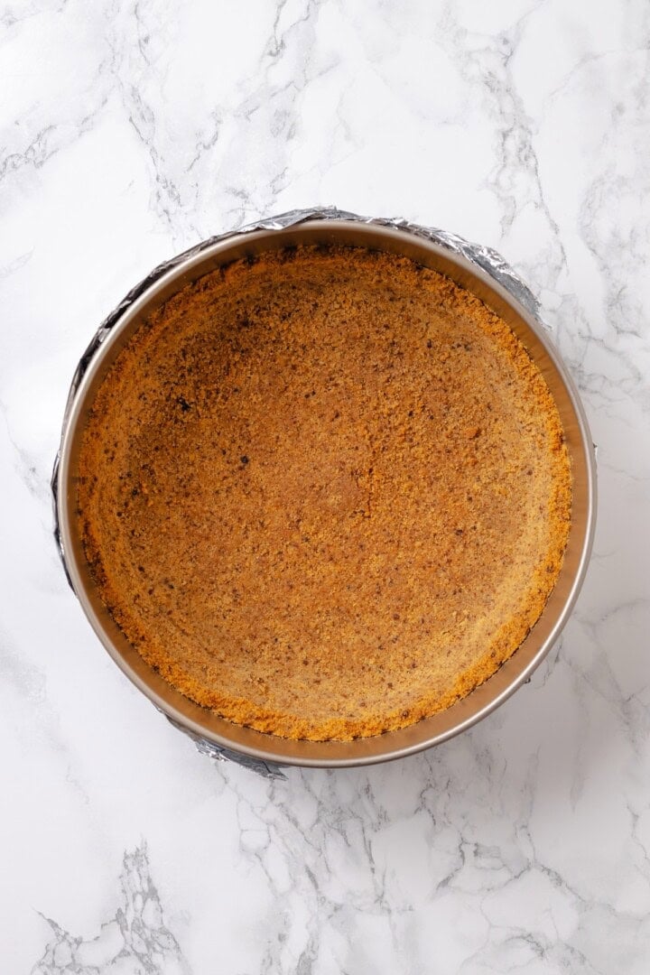 With a brown sugar cinnamon swirl and cream cheese frosting, this cinnamon roll cheesecake recipe is cozy and decadent at the same time! Overhead view of graham cracker crust in springform pan