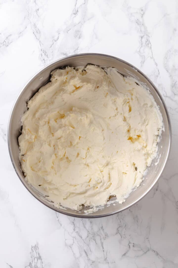 With a brown sugar cinnamon swirl and cream cheese frosting, this cinnamon roll cheesecake recipe is cozy and decadent at the same time! Overhead view of beaten vegan cream cheese in mixing bowl