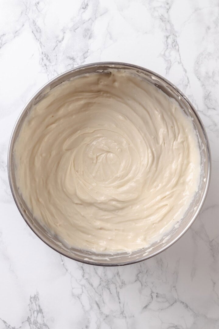 With a brown sugar cinnamon swirl and cream cheese frosting, this cinnamon roll cheesecake recipe is cozy and decadent at the same time! Overhead view of vegan cheesecake mixture in mixing bowl