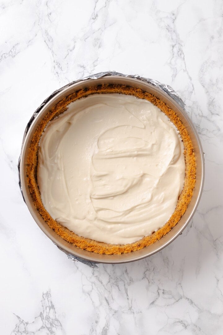 With a brown sugar cinnamon swirl and cream cheese frosting, this cinnamon roll cheesecake recipe is cozy and decadent at the same time! Overhead view of vegan cheesecake mixture added to crust