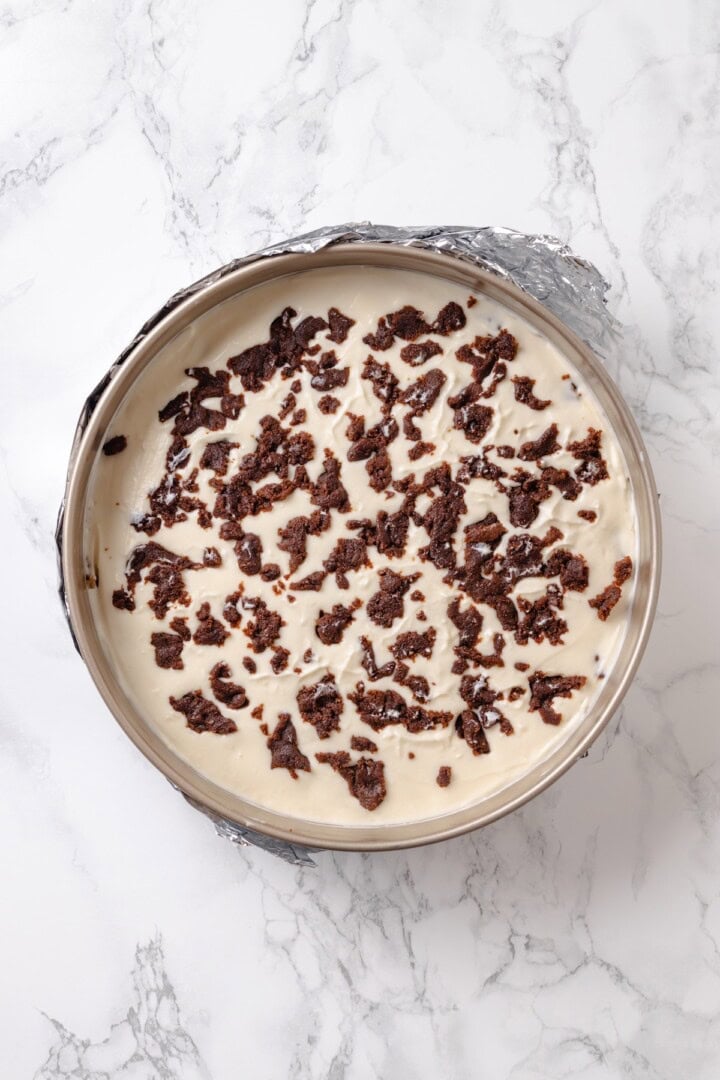 With a brown sugar cinnamon swirl and cream cheese frosting, this cinnamon roll cheesecake recipe is cozy and decadent at the same time! Overhead view of unbaked cinnamon roll cheesecake in springform pan