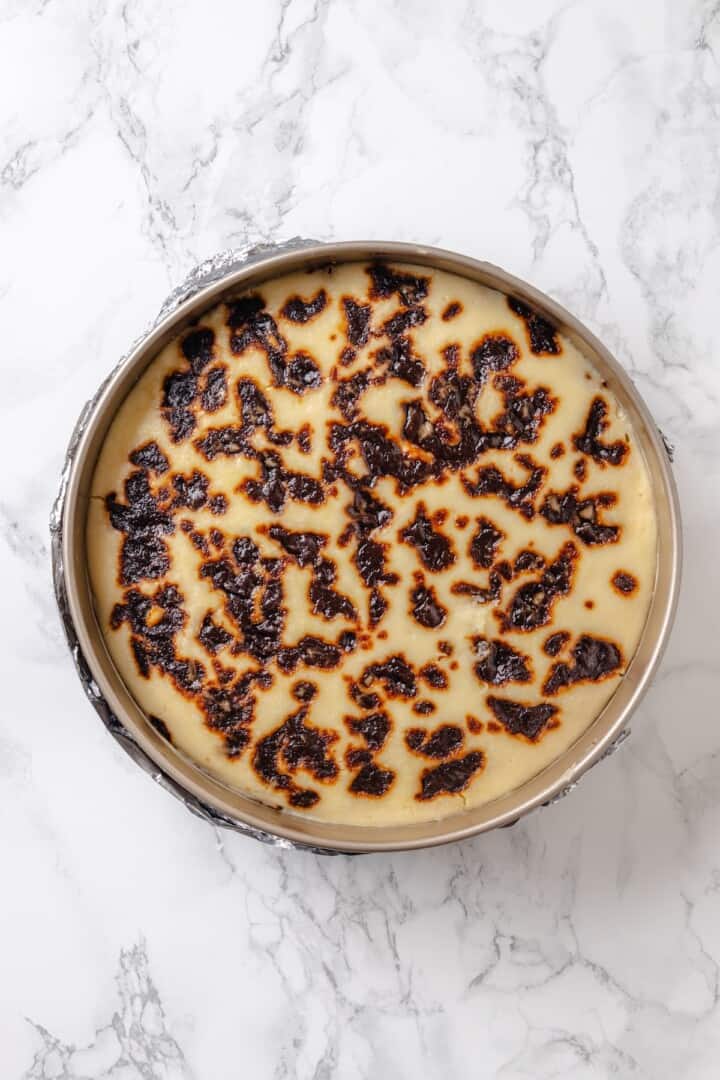 With a brown sugar cinnamon swirl and cream cheese frosting, this cinnamon roll cheesecake recipe is cozy and decadent at the same time! Overhead view of baked cinnamon roll cheesecake in springform pan