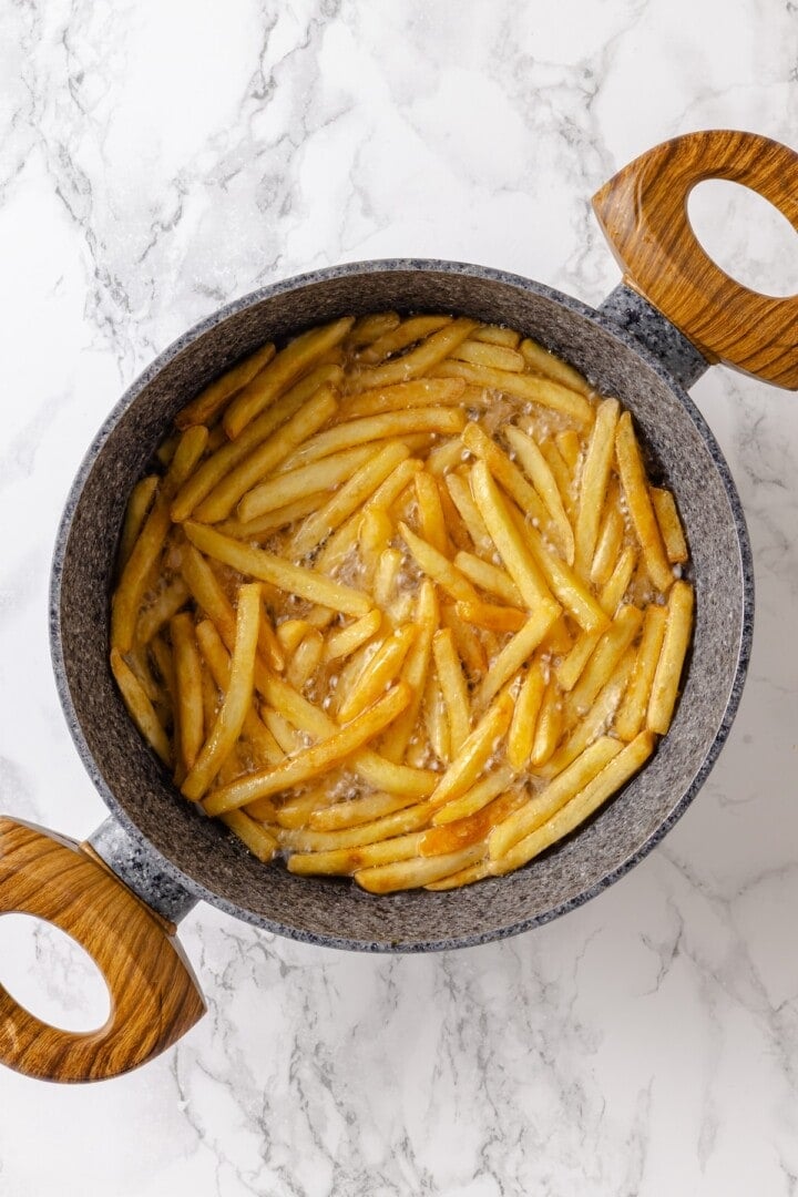 Whether you bake them or deep fry them, these crispy Garlic Fries are guaranteed to be a hit! They're cheesy, easy and packed with flavour. Overhead view of fries cooking in oil