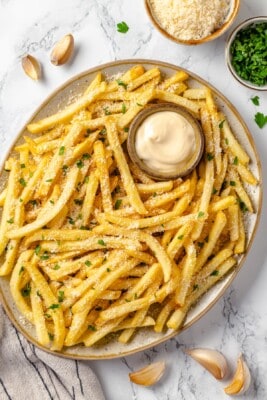 Overhead view of garlic fries on platter with bowl of aioli