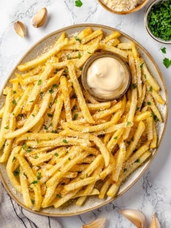 Overhead view of garlic fries on platter with bowl of aioli