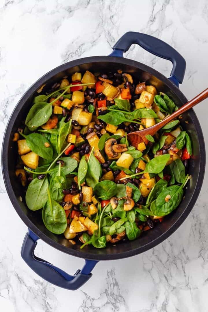 Overhead view of spinach added to skillet of breakfast hash
