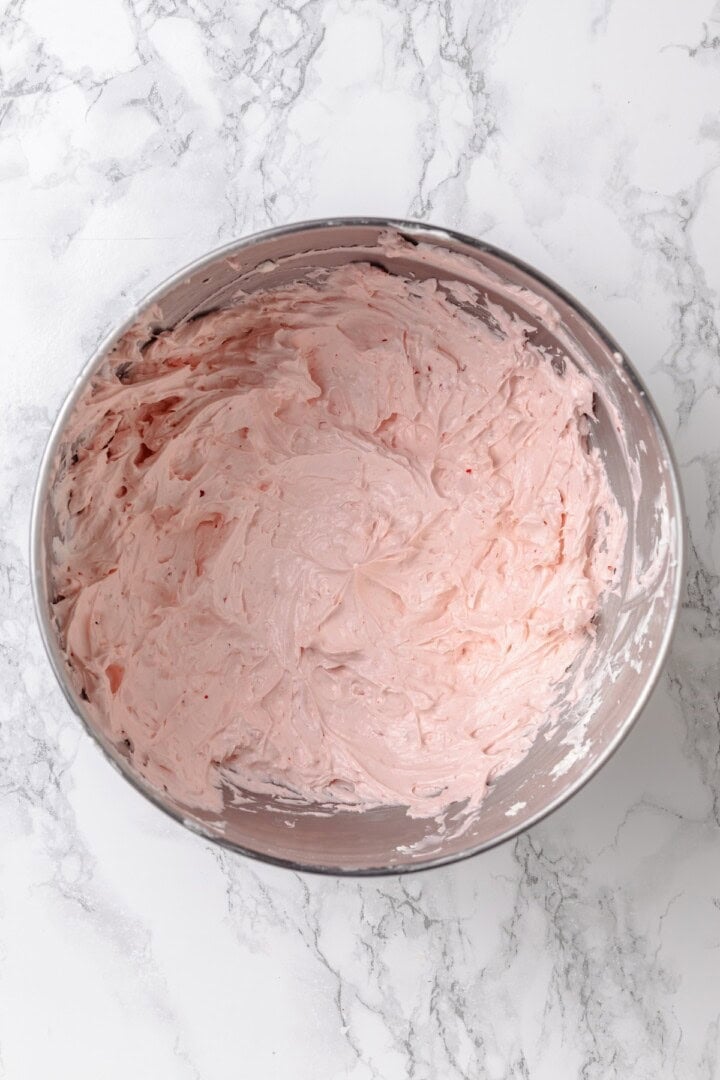 Fluffy chocolate cake, a jammy strawberry filling, strawberry buttercream and chocolate ganache make this Chocolate Strawberry Cake the best! Overhead view of strawberry buttercream frosting in bowl