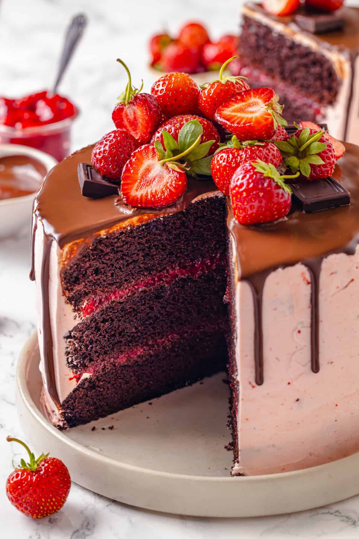 Fluffy chocolate cake, a jammy strawberry filling, strawberry buttercream and chocolate ganache make this Chocolate Strawberry Cake the best! Chocolate strawberry cake on platter with slice removed to show layers