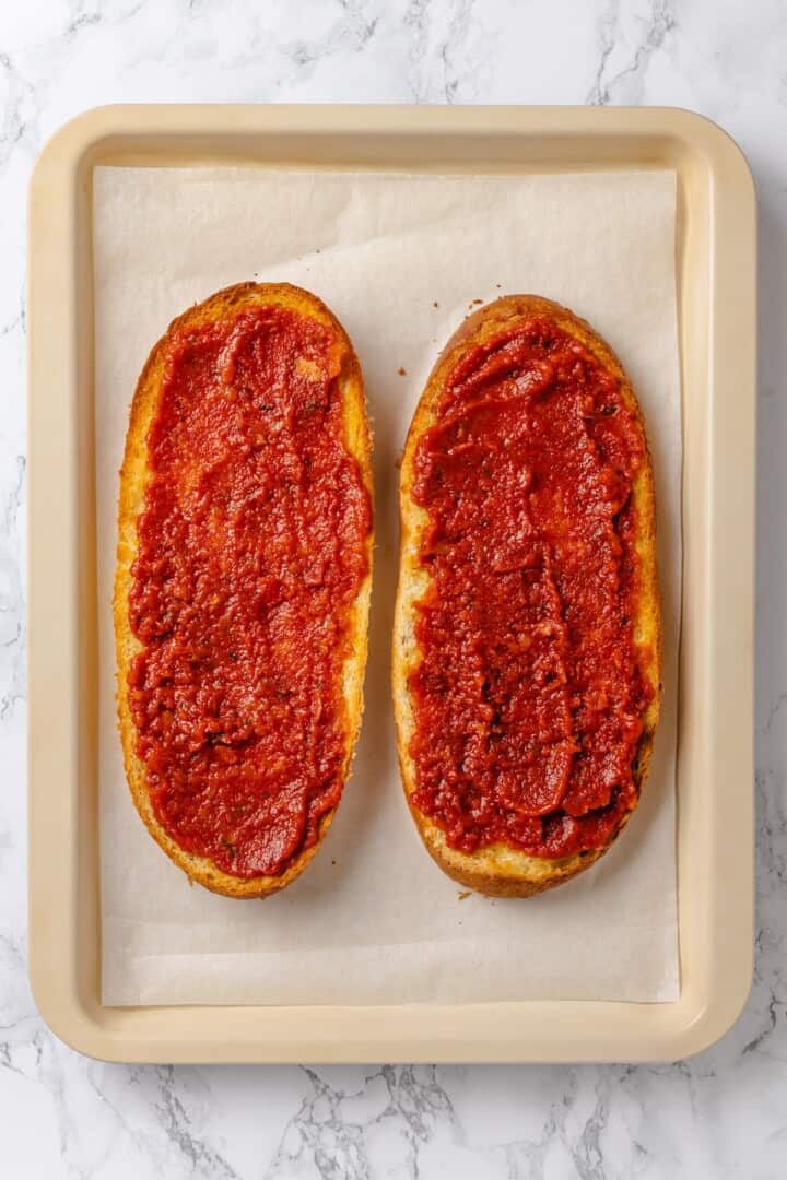 Overhead view of two French bread halves topped with pizza sauce