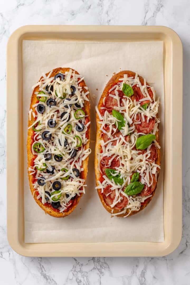 Two unbaked French bread pizzas on sheet pan