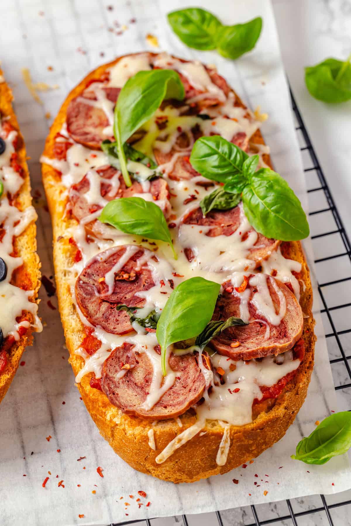 Fresh basil leaves scattered over vegan French bread pizza topped with salami