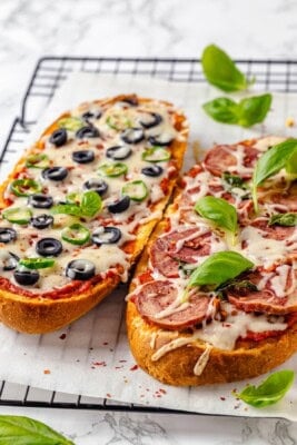 Two vegan French bread pizzas on wire rack with fresh basil
