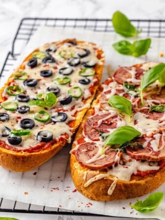 Two vegan French bread pizzas on wire rack with fresh basil