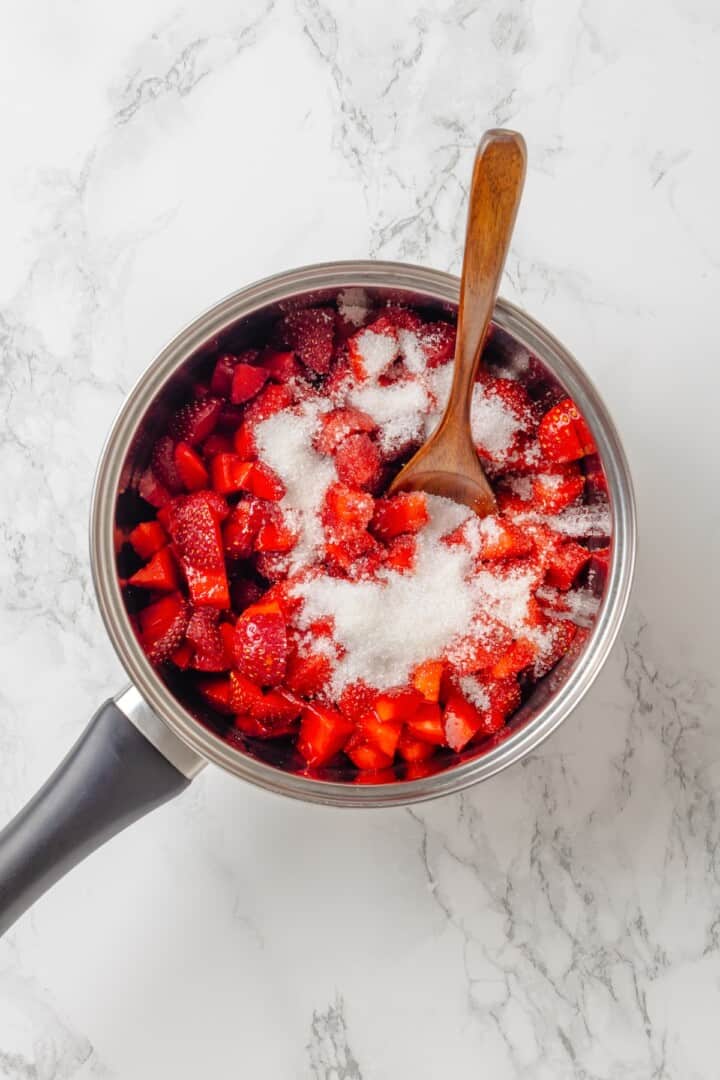 Spoon stirring sugar into strawberries in pan