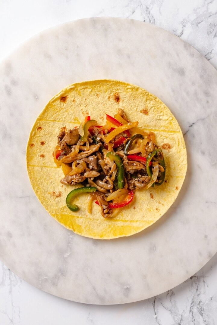 These crispy Tofu Tacos are topped with meaty fajita mushrooms and veggies for a vegan taco recipe that’s satisfying and delicious! Overhead view of mushroom fajitas added to tortilla