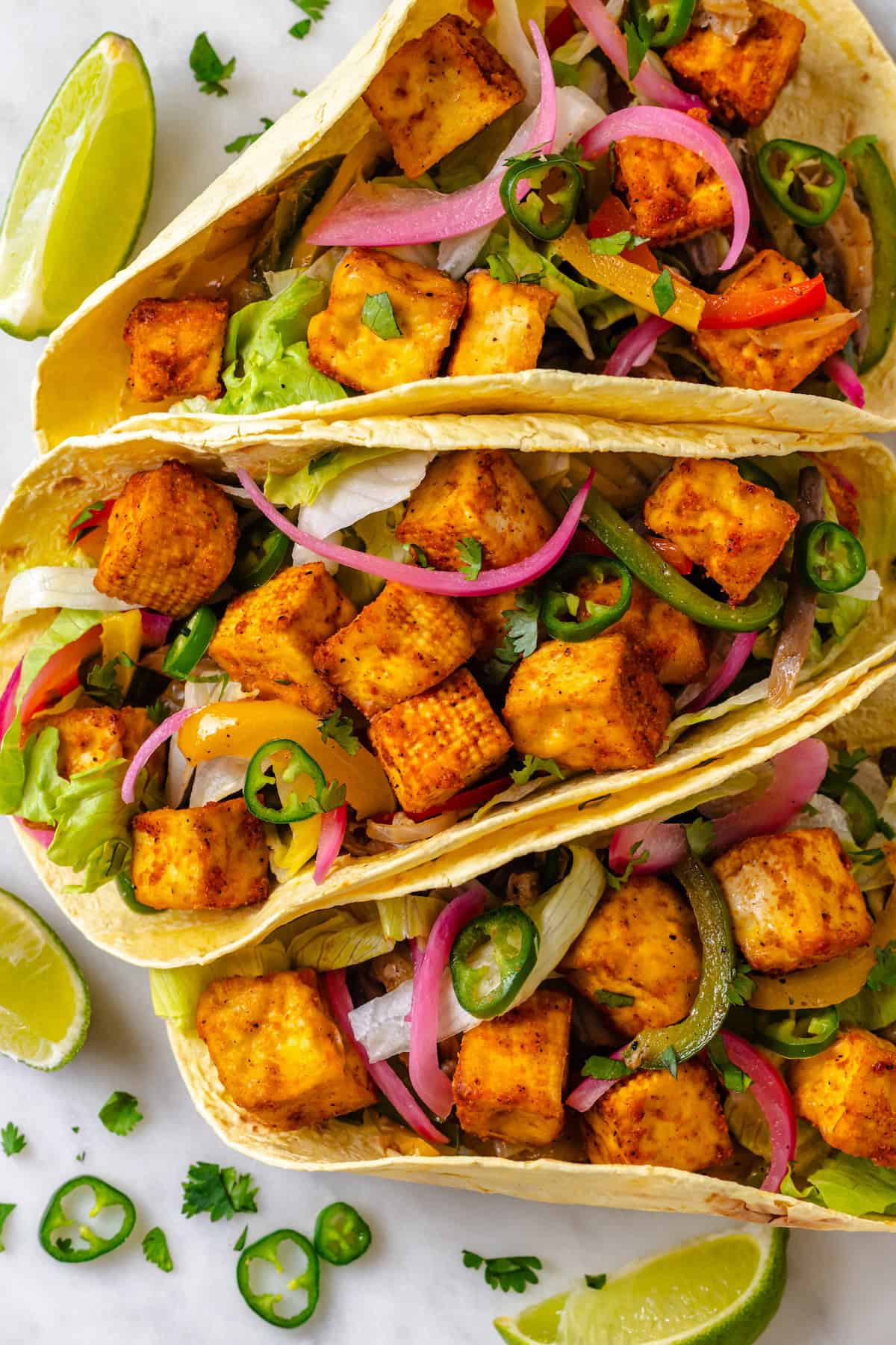 These crispy Tofu Tacos are topped with meaty fajita mushrooms and veggies for a vegan taco recipe that’s satisfying and delicious! Overhead view of 3 vegan tofu tacos with fajita vegetables