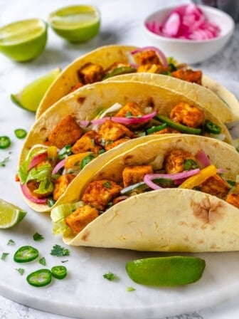 Three tofu tacos lined up on marble tray
