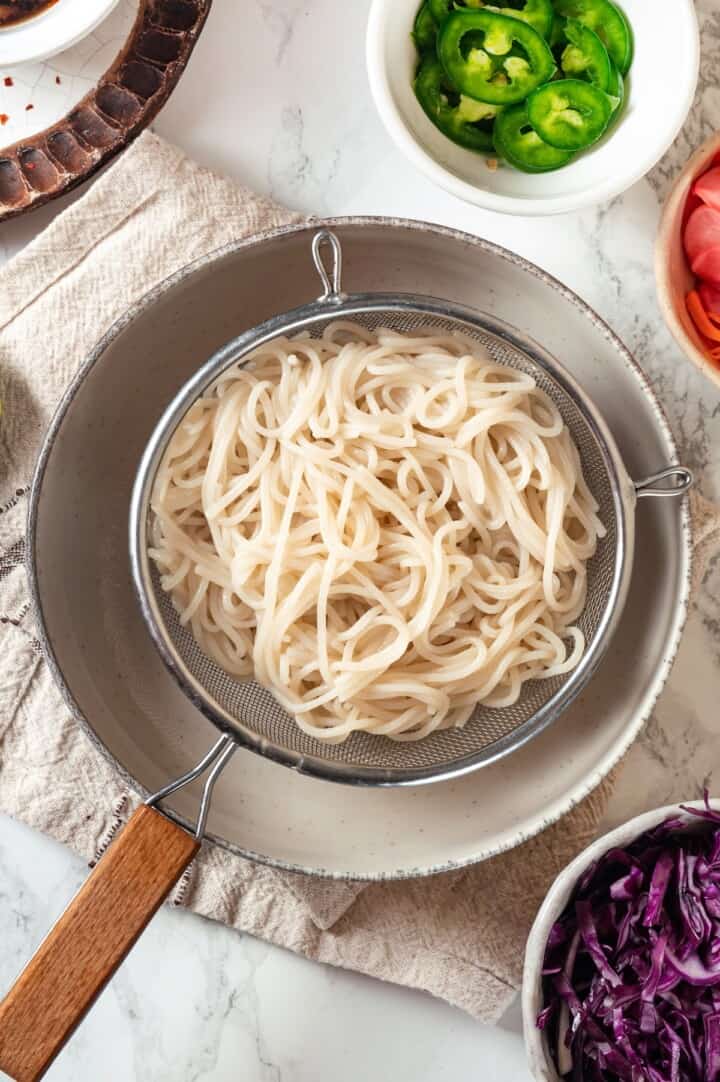Drained rice noodles over pot.