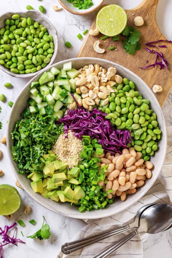 Overhead view of ingredients for edamame salad in bowl before mixing.