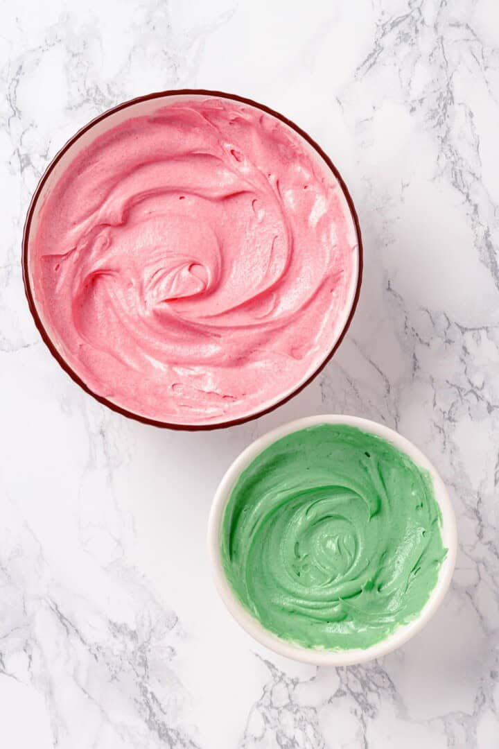 Bowl of green frosting and bowl with pink frosting.