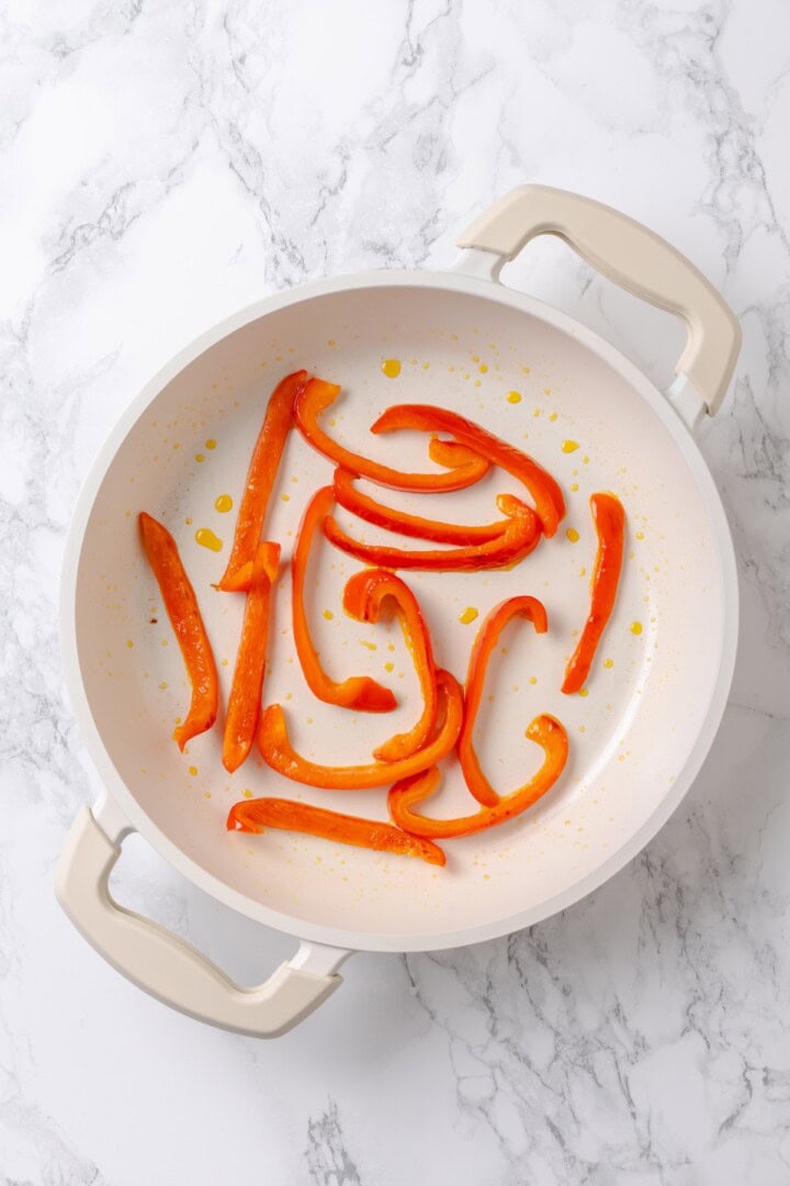 Overhead view of red pepper strips cooking in pan