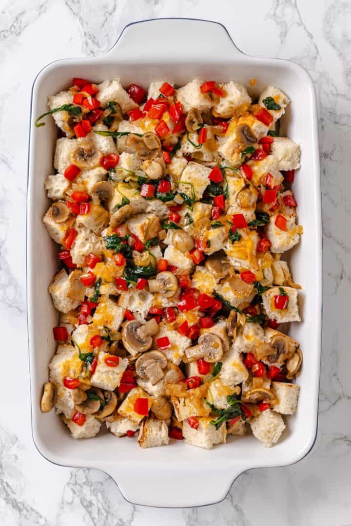 Bread and vegetables added to baking dish for strata