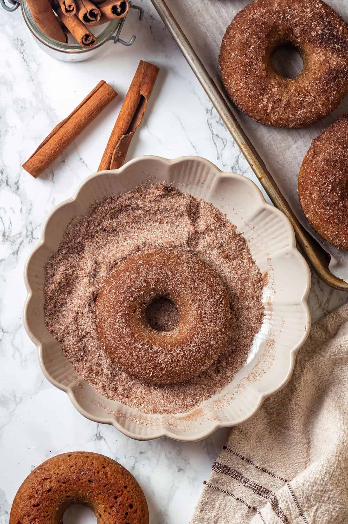 Vegan apple cider donuts in plate of cinnamon sugar.