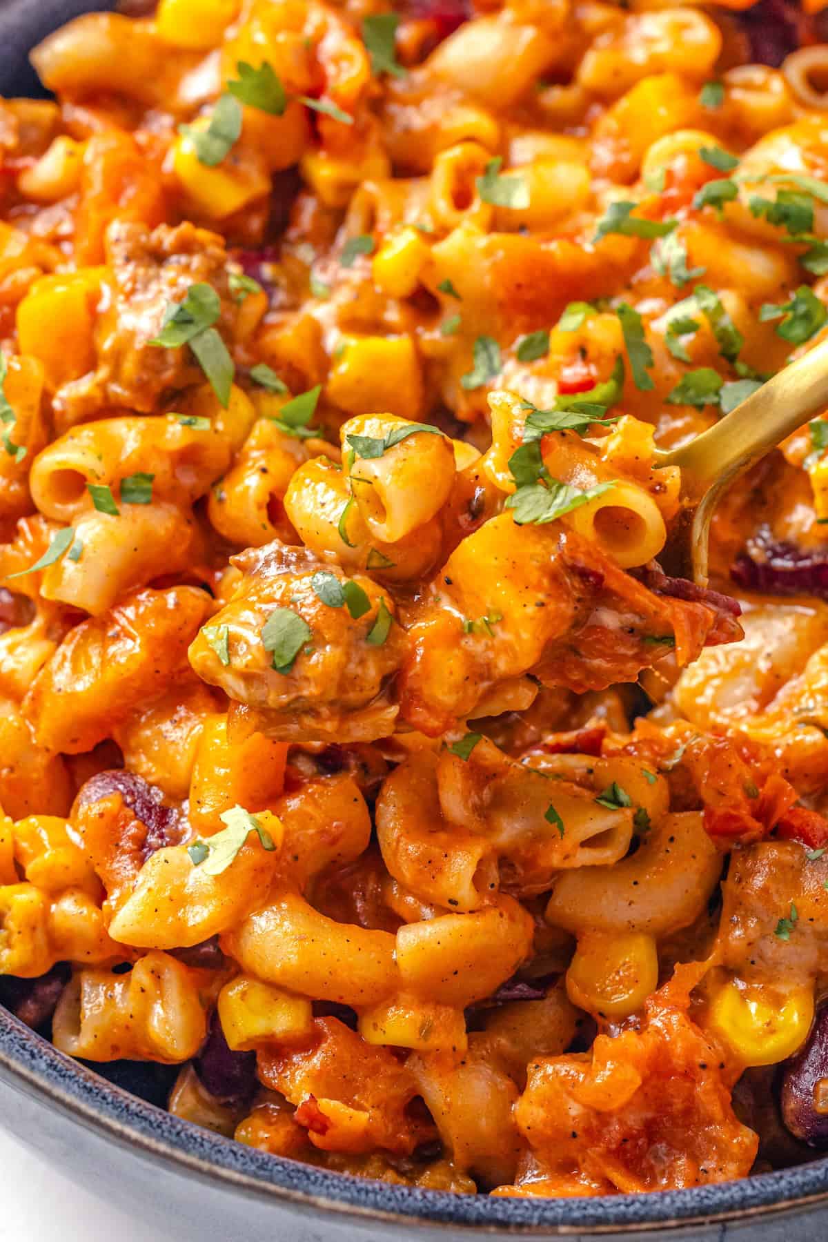 Spoon digging into bowl of chili mac and cheese.
