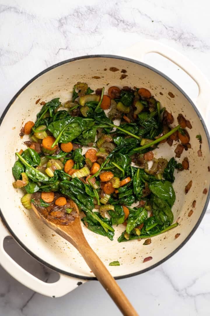 Eliminate waste and make a delicious dinner with this Broccoli Fridge Clean-Out Soup! Rich and creamy, with optional grilled cheese croutons. Stirring greens with mirepoix in Dutch oven.