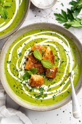 Bowl of broccoli fridge clean-out soup with grilled cheese croutons and swirl of coconut cream.